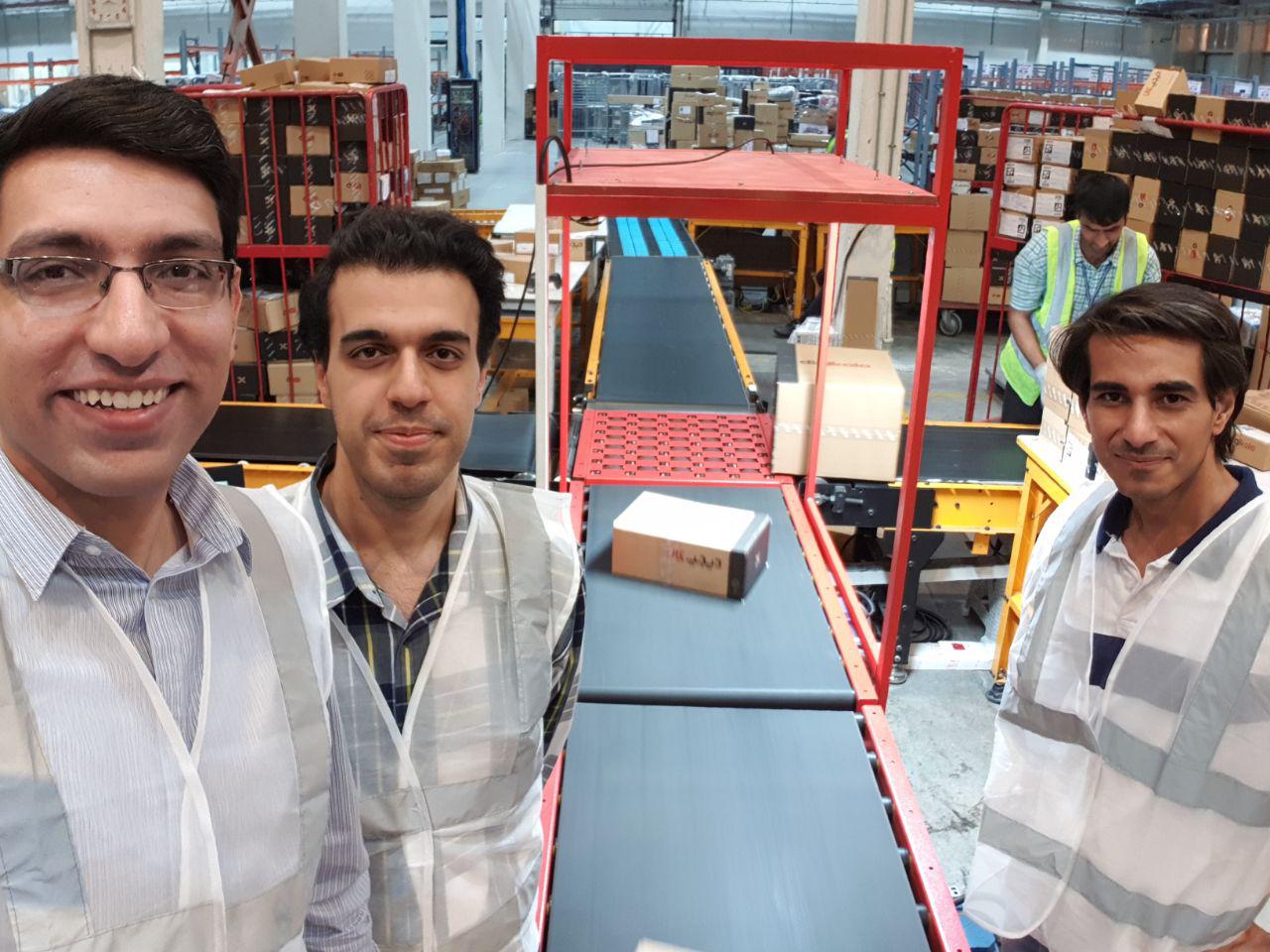 Farzad and two colleagues beside the parcel sorter conveyor in a Digikala warehouse