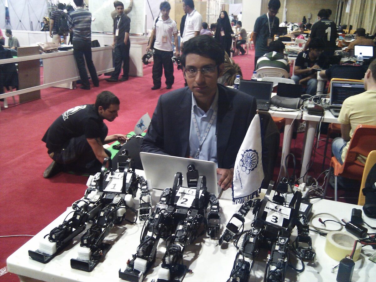 Three numbered kid-size humanoid robots lined up on the team bench at a RoboCup competition