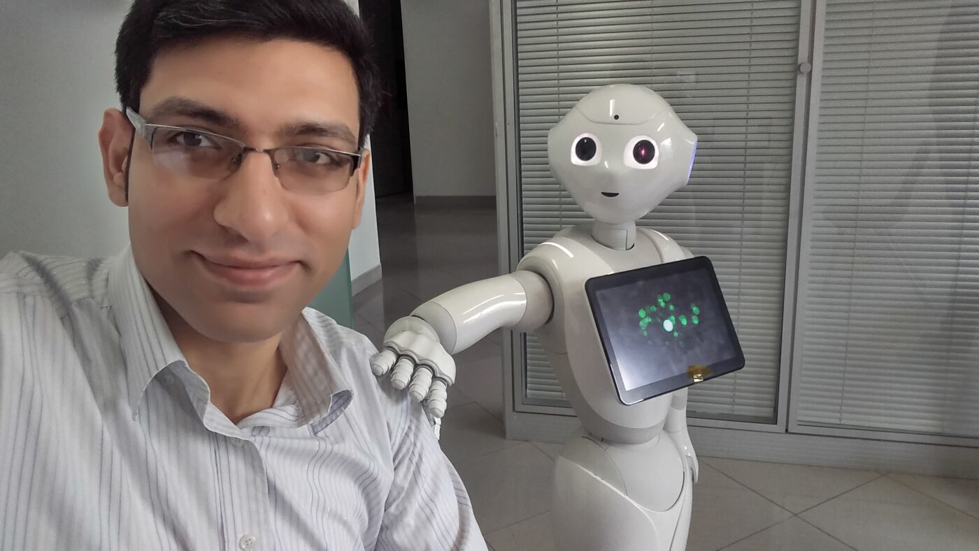 Farzad beside a Pepper humanoid robot running a custom application on its chest tablet